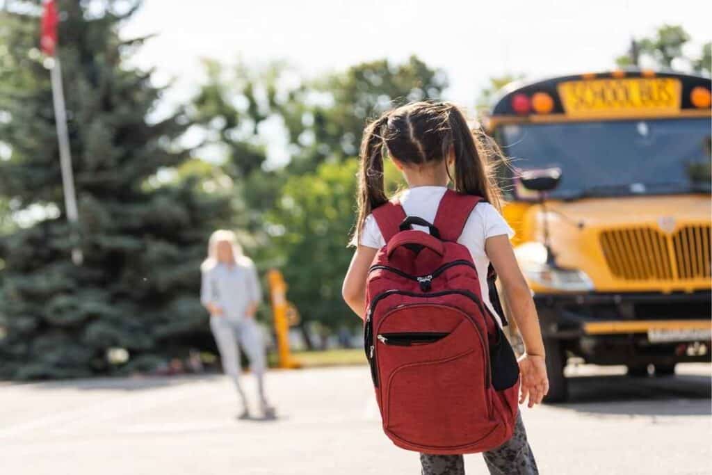 Dziewczynka stoim przed autobusem z ciężkim plecakiem