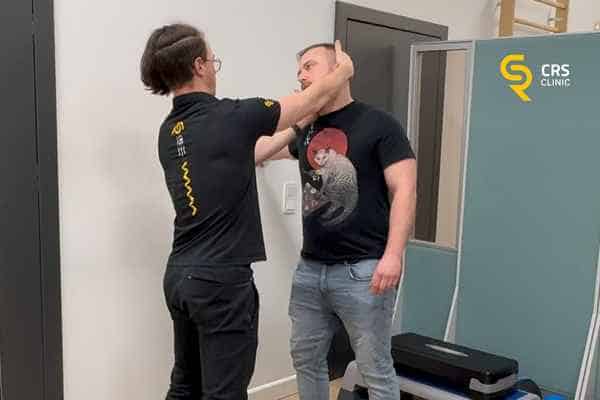 Fizjoterapeuta pokazuje pacjentowi z cieśnią nadgarstka ćwiczenia na kark i cały nerw w CRS Clinic Warszawa